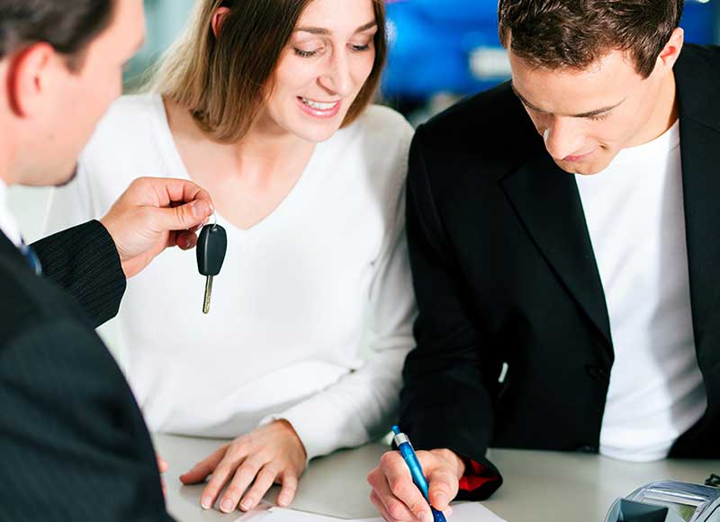 Car salesman handing keys to young couple
